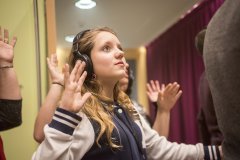 A teenage girl wearing headphones as part of an interactive theatre piece holds her hands in the air.